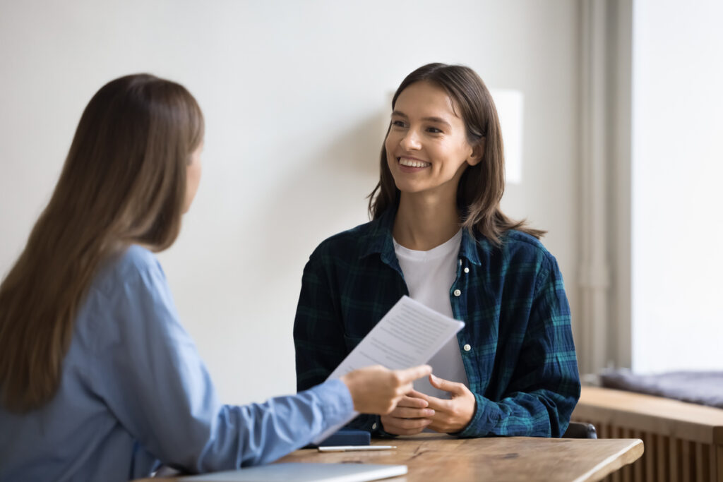 Happy young first homebuyers candidate woman in informal clothes talking to employee on interview, talking to boss with toothy smile, meeting with a mortgage broker